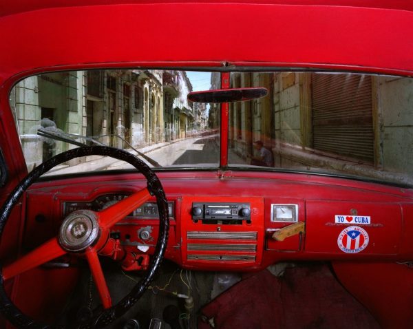 Alex Harris, a car interior with a red dashboard and a sticker reading Yo Cuba, a street of shuttered buildings beyond the windscreen
