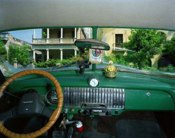 Alex Harris, a car interior with a green dashboard and a laced steering wheel, a colonnaded building beyond the windscreen