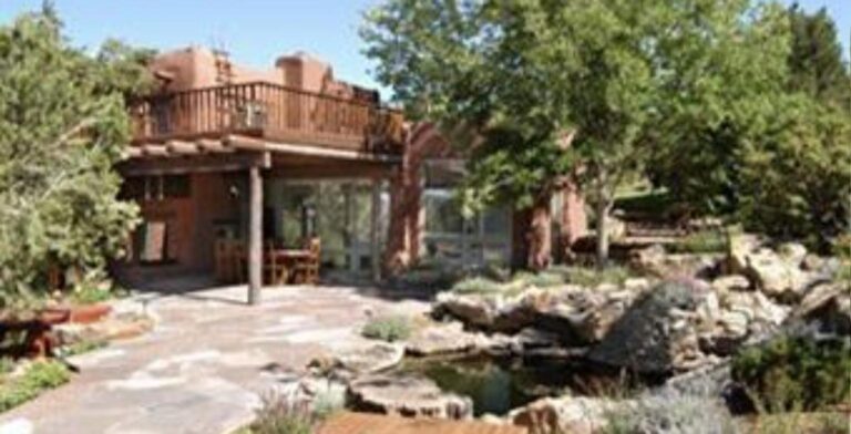 Adobe house at 1 Caminito del Angel in Tesuque with a rooftop deck, a covered portal, a flagstone patio, and a rock lined pond