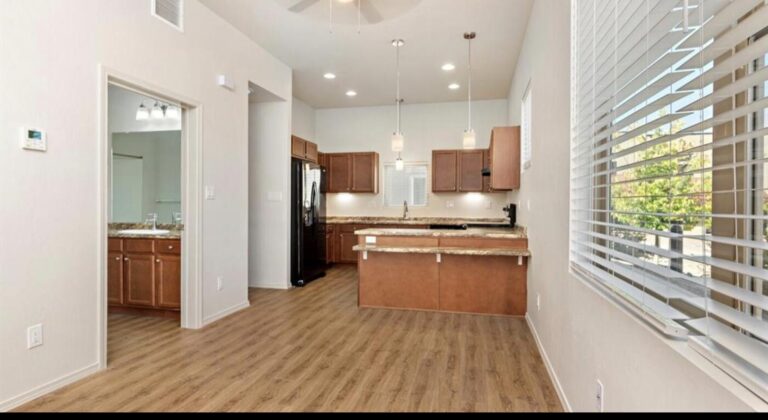 Open living area with luxury vinyl plank floors looking through to the kitchen and a tall window at 1113 Paseo Corazon #201, Santa Fe