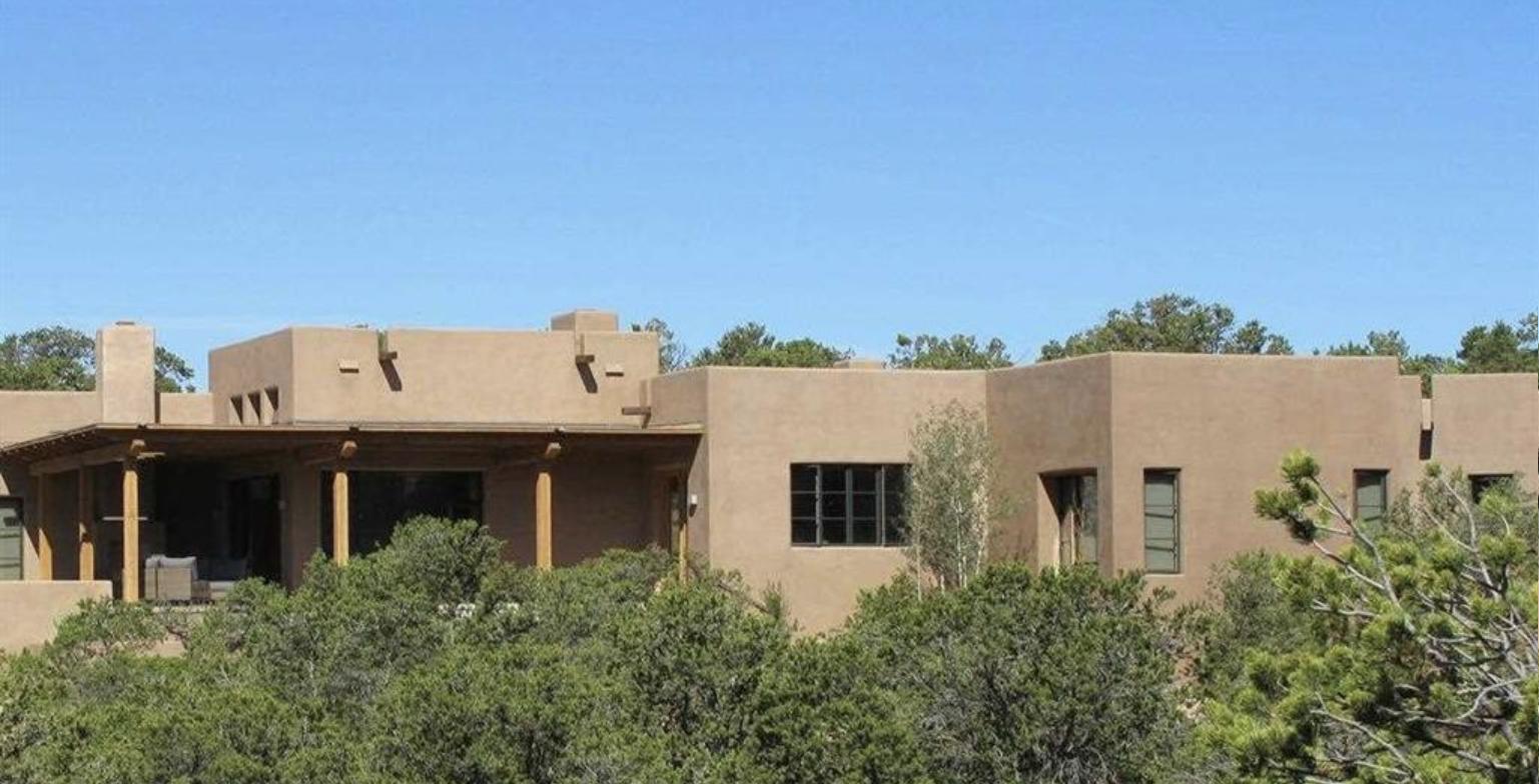 Casa Carolina at 129 Circle Drive, a contemporary Pueblo style house with a covered portal and stepped parapets above pinon and juniper under a blue sky