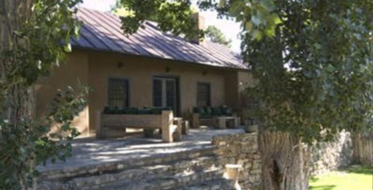 Adobe farmhouse with a standing seam roof, a stone terrace with benches, and a large cottonwood at 1520 Cerro Gordo