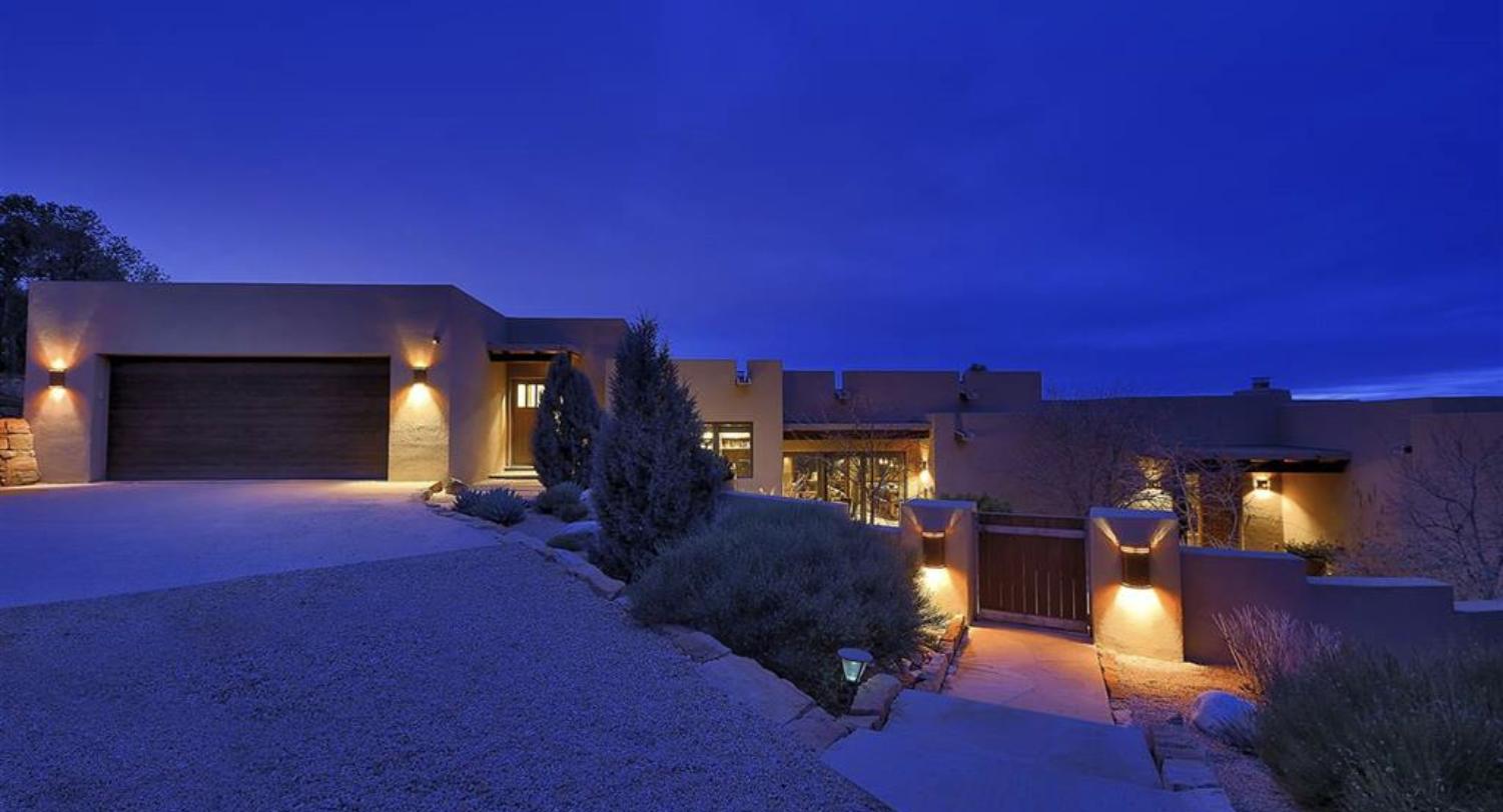Contemporary house lit at dusk with gated entry and garage at 1862 Camino Cruz Blanca, Ponderosa Ridge, Santa Fe