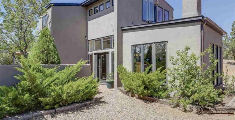 Two story stucco contemporary house at 19 Piute with clerestory windows, a glass entry, and junipers along a gravel walk