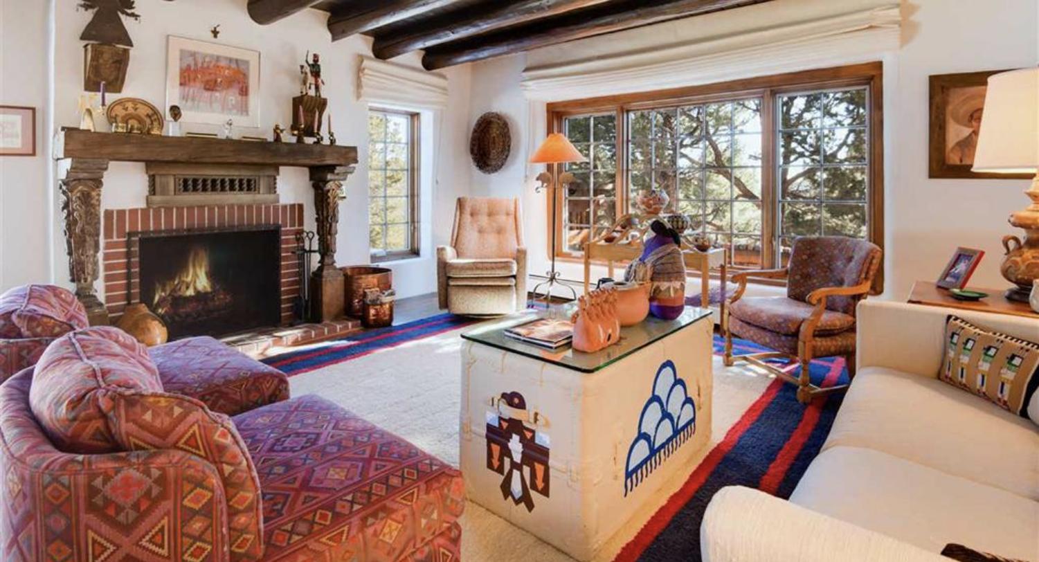 Living room with a carved wood mantel, vigas, and Navajo rugs at 2137 Paseo Ponderosa, Hyde Park Estates, Santa Fe