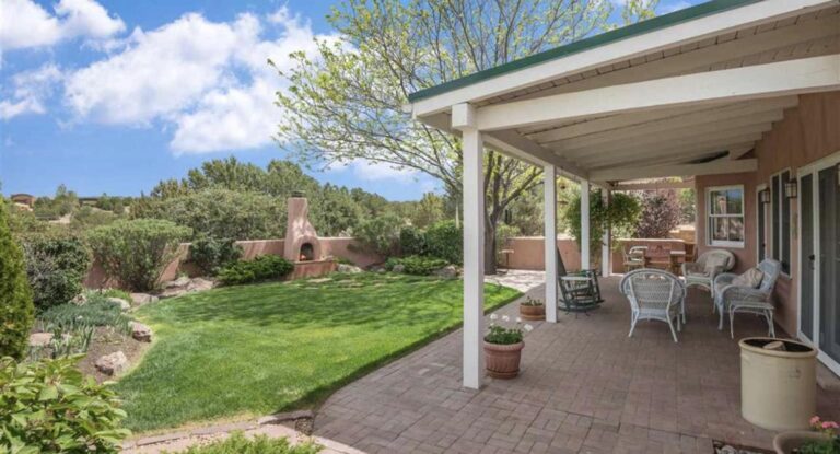 Covered portal looking onto a lawn, garden, and outdoor kiva fireplace at 30 Estrada Calabasa, La Tierra, Santa Fe