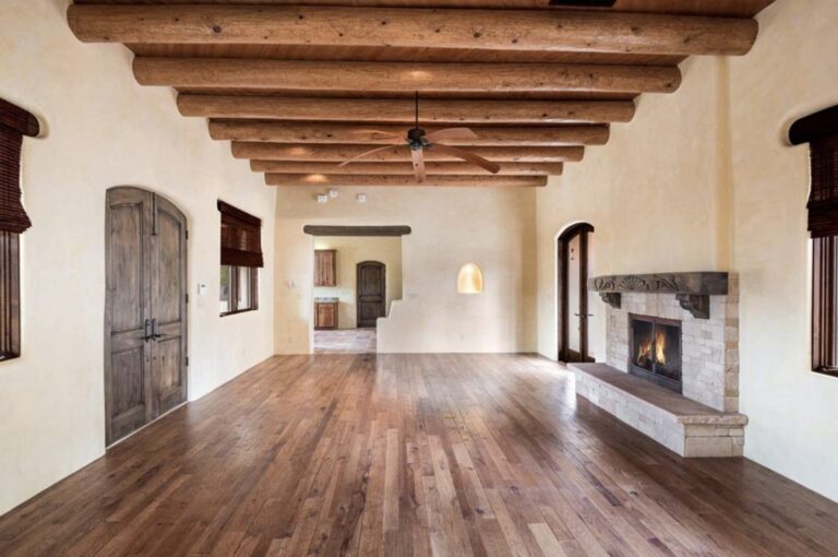 Living room with vigas, plaster walls, and a stone fireplace at 304 Callecita, Santa Fe