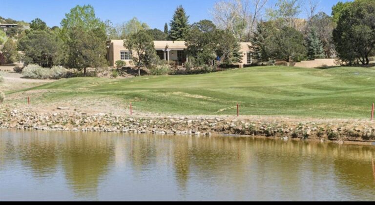 The hacienda at 3101 Old Pecos Trail #612 seen across the first fairway and pond at Quail Run, Santa Fe