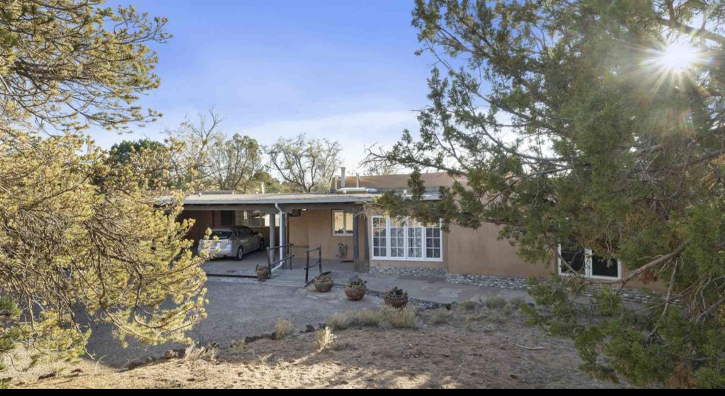Single level adobe house with carport seen through pinon at 3990 Old Santa Fe Trail, Santa Fe