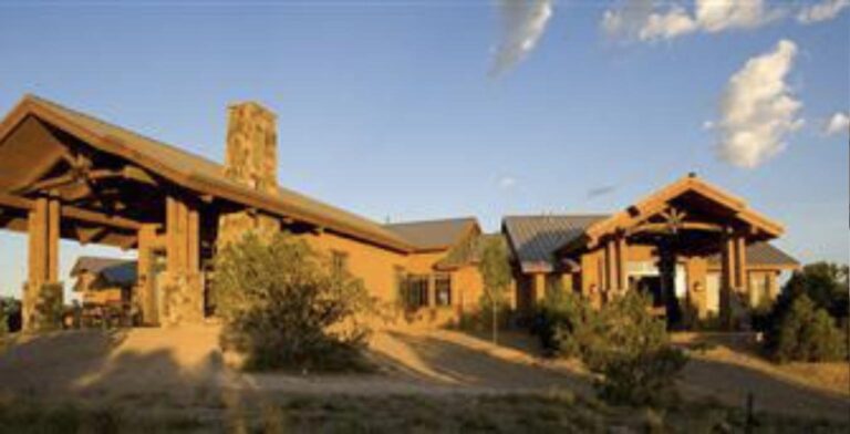 Timber framed portals and a stone chimney at 4 Camino Villenos in Las Campanas, lit by low evening sun under a blue sky