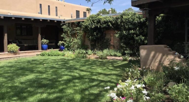 Walled courtyard with lawn, portal, and flowering borders at 632 Camino Lejo, Museum Hill, Santa Fe