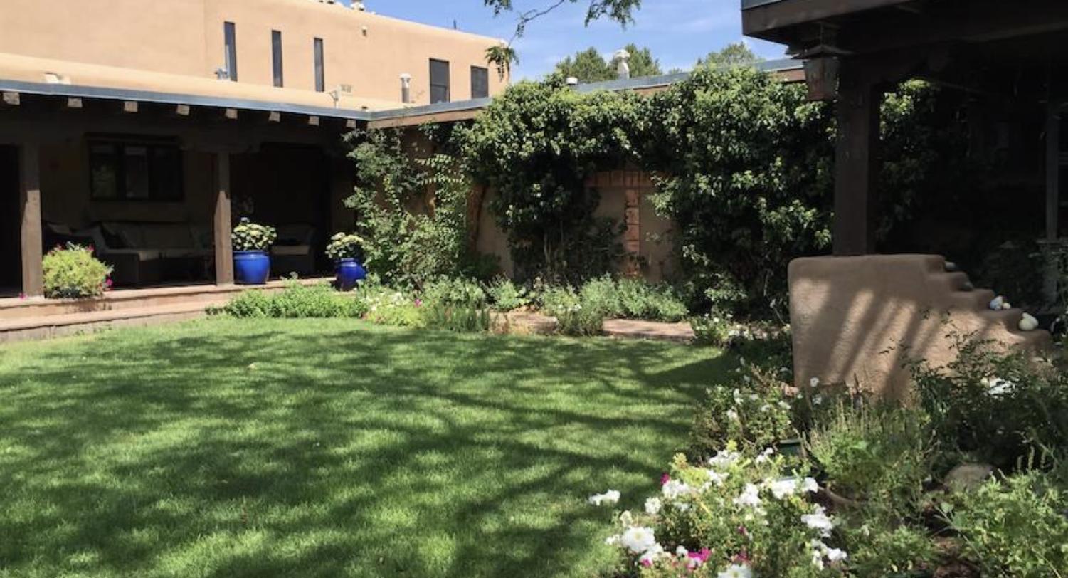 Walled courtyard with lawn, portal, and flowering borders at 632 Camino Lejo, Museum Hill, Santa Fe