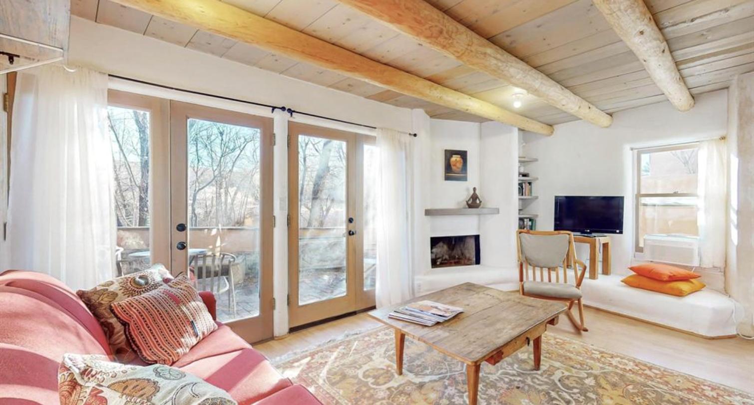 Living room with vigas, a kiva fireplace, and French doors onto the courtyard at 634 Garcia Street #25, Santa Fe