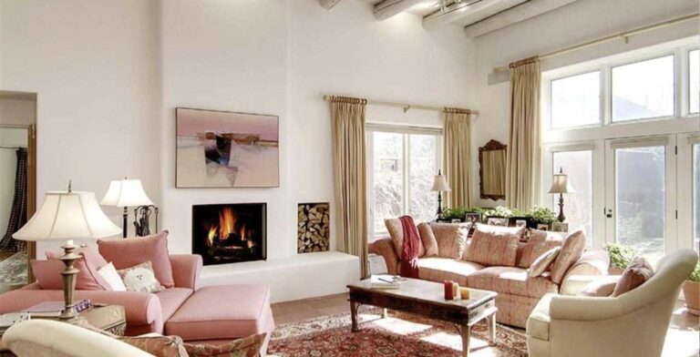 Living room at 748 Camino Mirada with a soaring white ceiling, a lit fireplace, tall windows, and rose colored sofas on a Persian rug