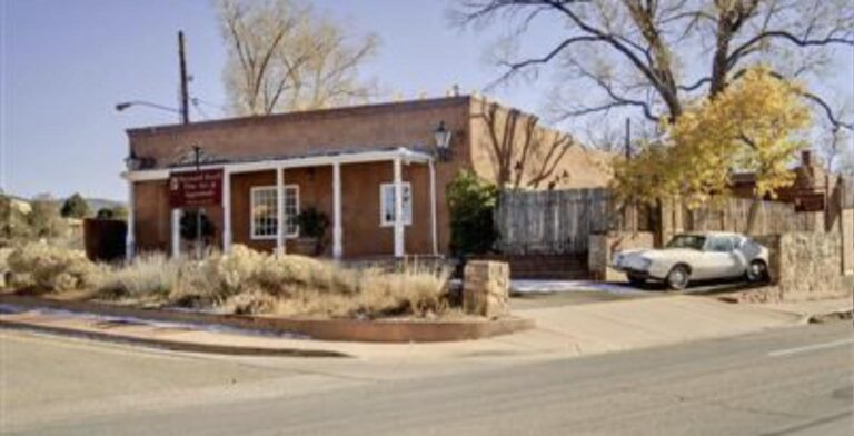 Adobe building with a white columned portal and a wooden fence at 806 Old Santa Fe Trail in autumn, with a car parked beside it