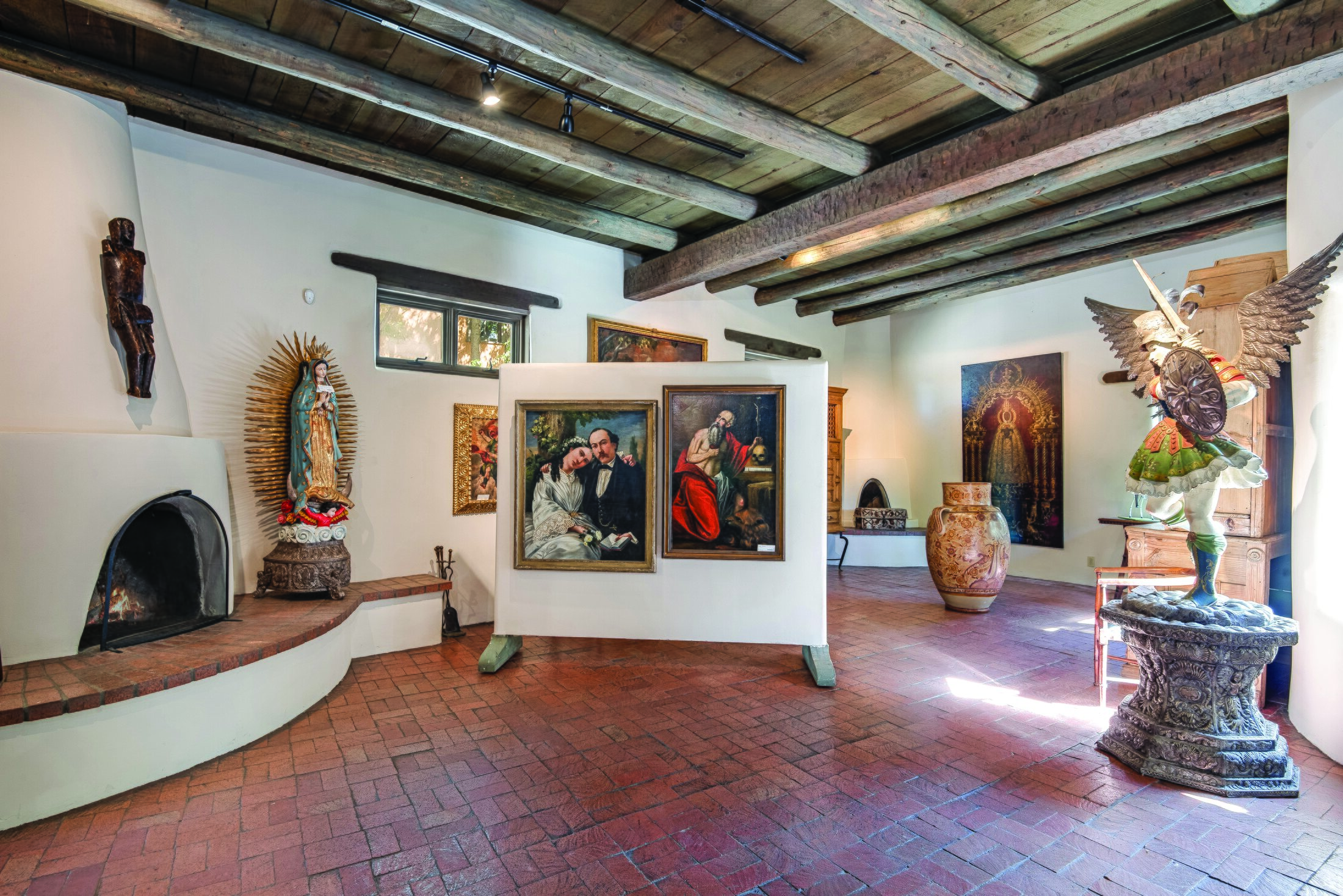 Art-filled adobe interior at 550 Canyon Road in Santa Fe, with vigas, brick floors, paintings and sculpture