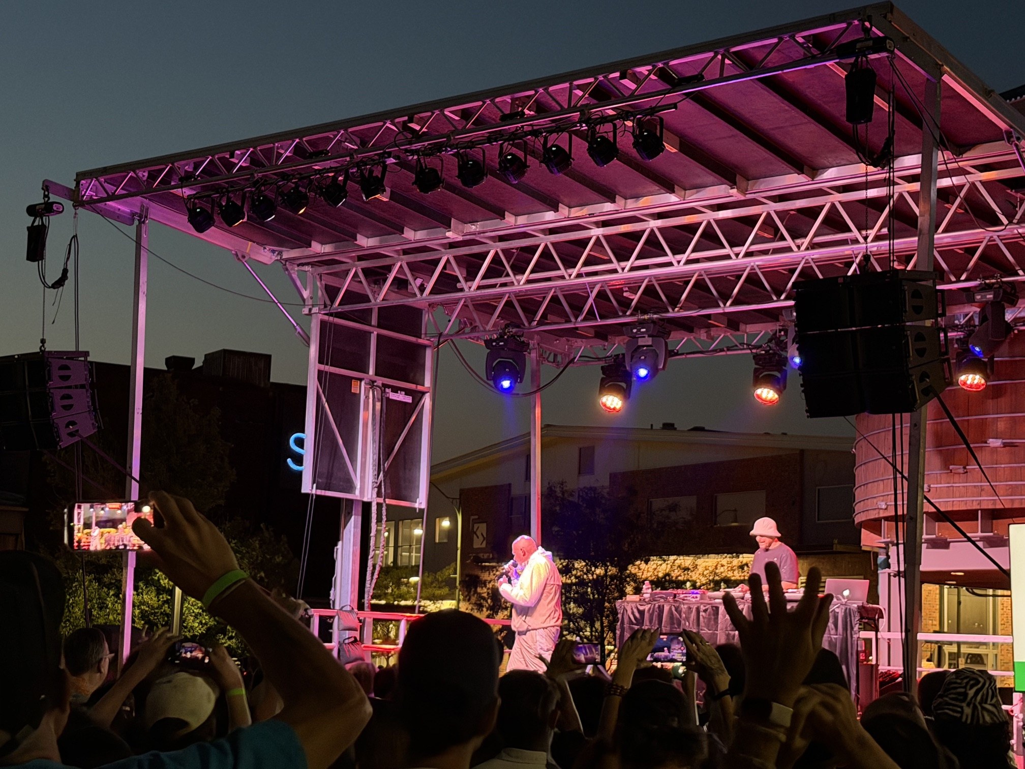 Brother Ali performing in white with a DJ under magenta stage lighting at Raashan Ahmad's Hip Hop Festival, Santa Fe Railyard, August 2026.