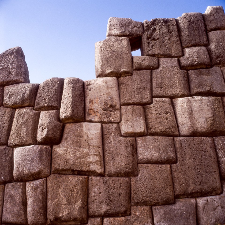 A wall of massive ancient dry-stone masonry, precisely fitted blocks laid without mortar, against a clear blue sky.