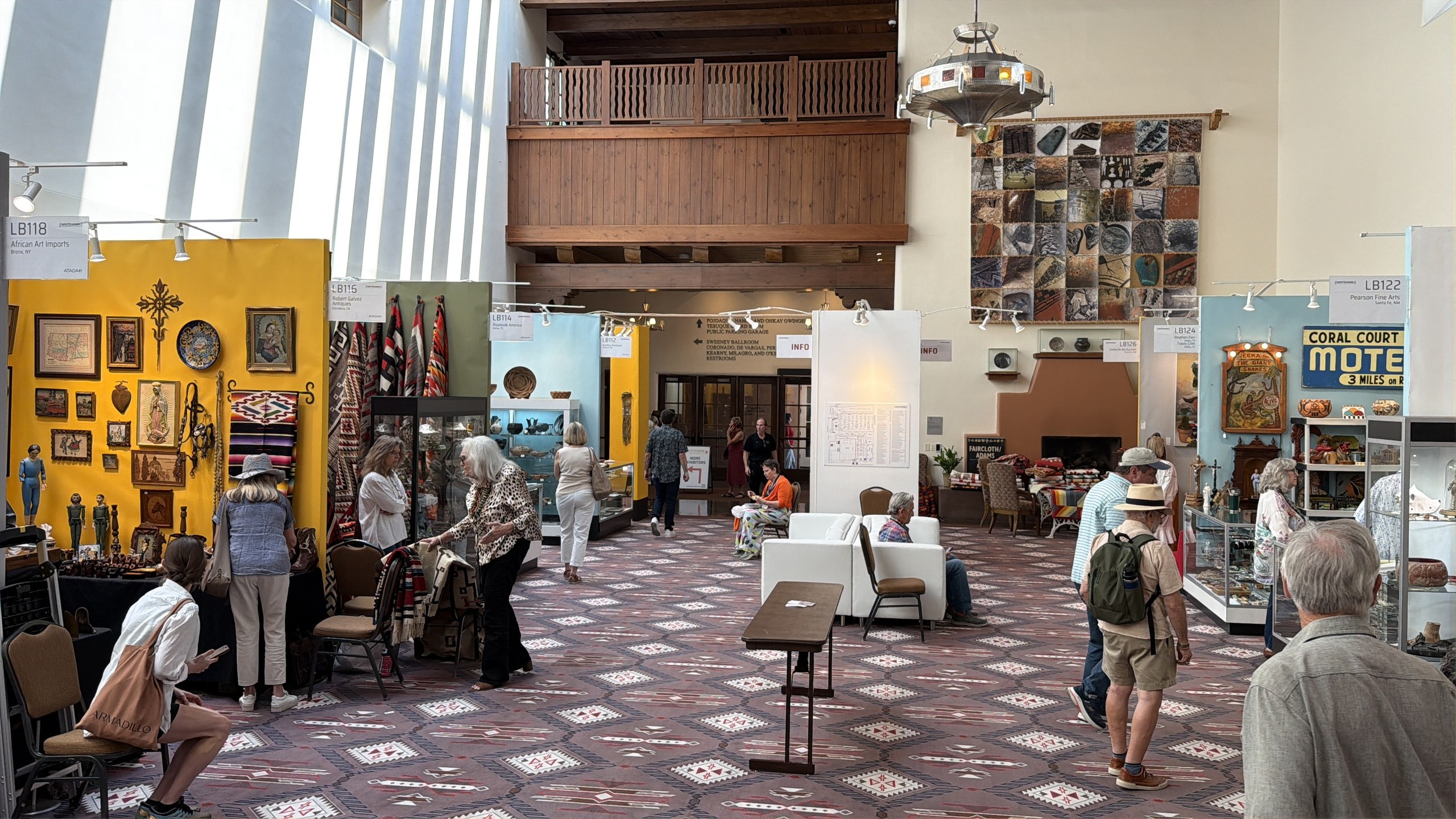 The lobby of the Santa Fe Community Convention Center during the 48th Whitehawk Antique Indian and Ethnographic Art Show, dealer booths lining the walls with textiles, pottery and folk art, August 2026.