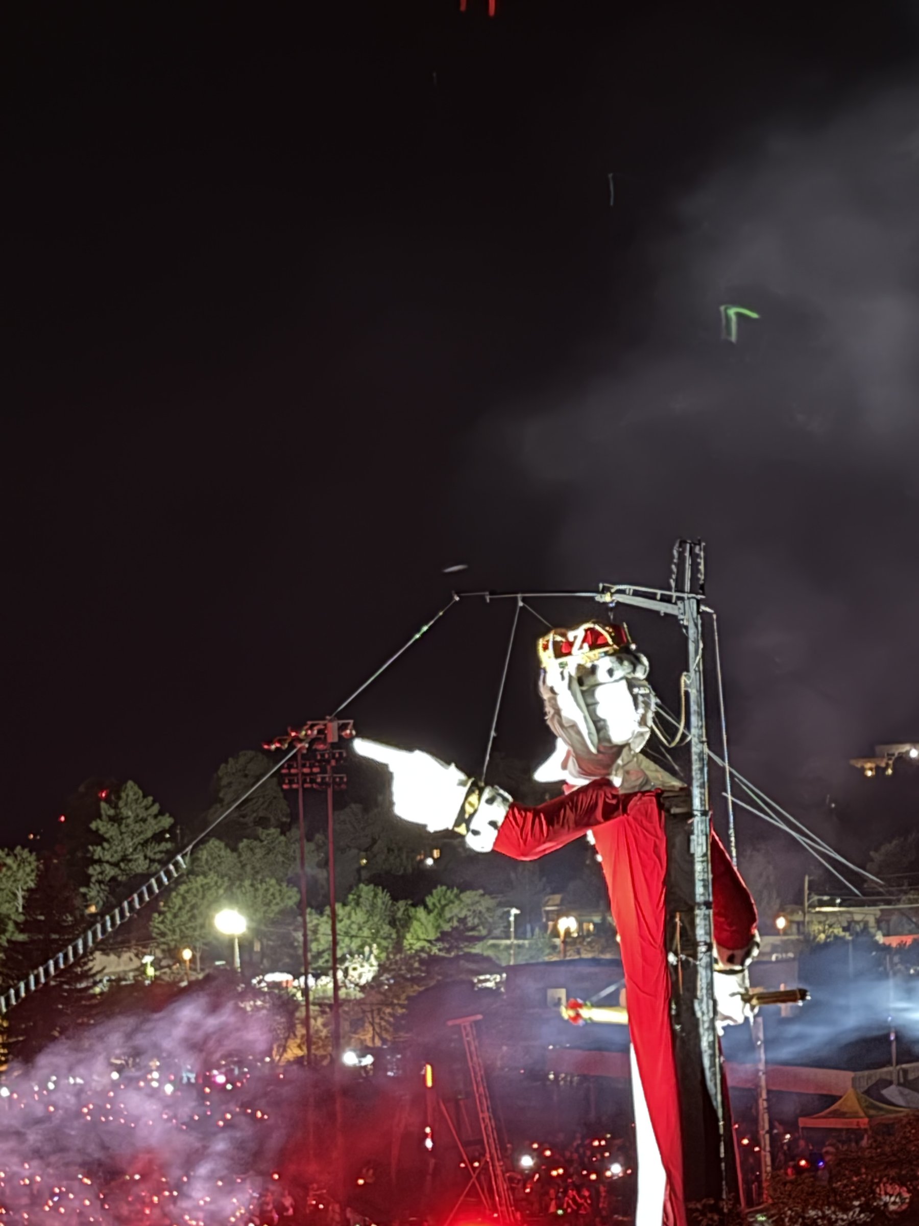 Zozobra dressed as King George III in a gold crown, white ermine robe, and red cape, lit against the night sky at Fort Marcy Park.